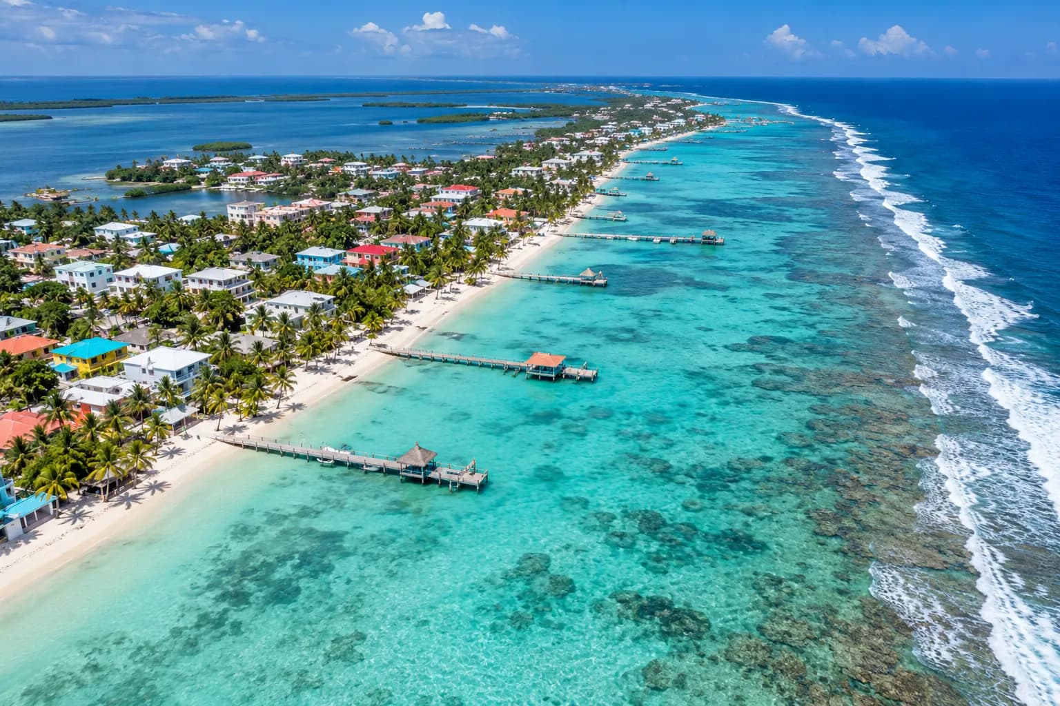 Aerial view of an Ambergris Caye beach with palm trees, wooden piers and the barrier reef offshore