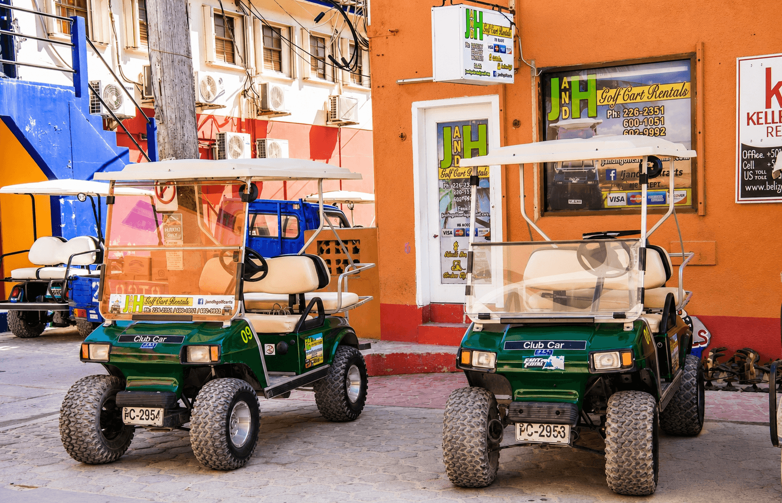 Two green J&H golf carts parked outside the J&H rental office on Barrier Reef Drive in San Pedro, Belize