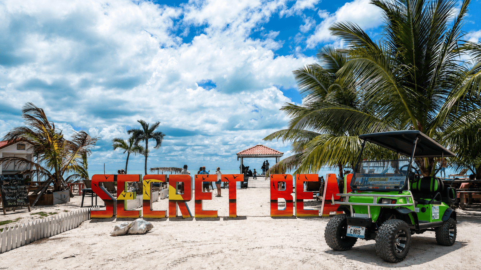 A green J&H golf cart parked beside the colorful Secret Beach sign on northern Ambergris Caye