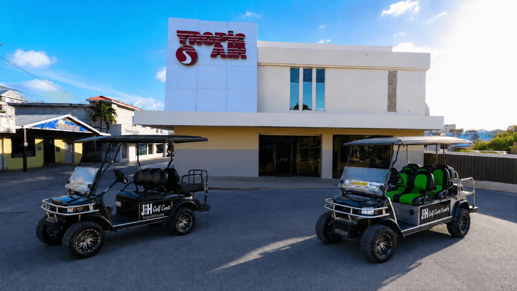 Two J&H golf carts parked in front of the Tropic Air terminal at the San Pedro airstrip on Ambergris Caye