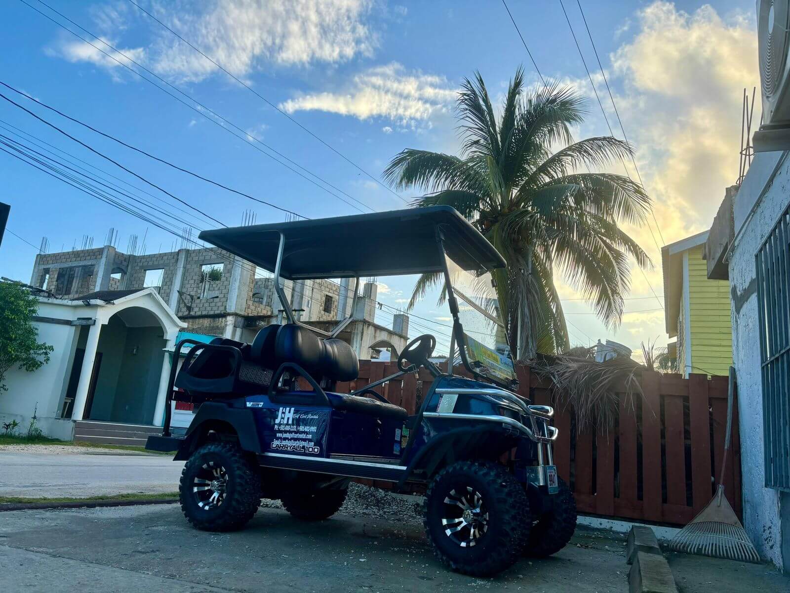 Blue 6-seater lifted golf cart parked under a palm tree in San Pedro, Belize