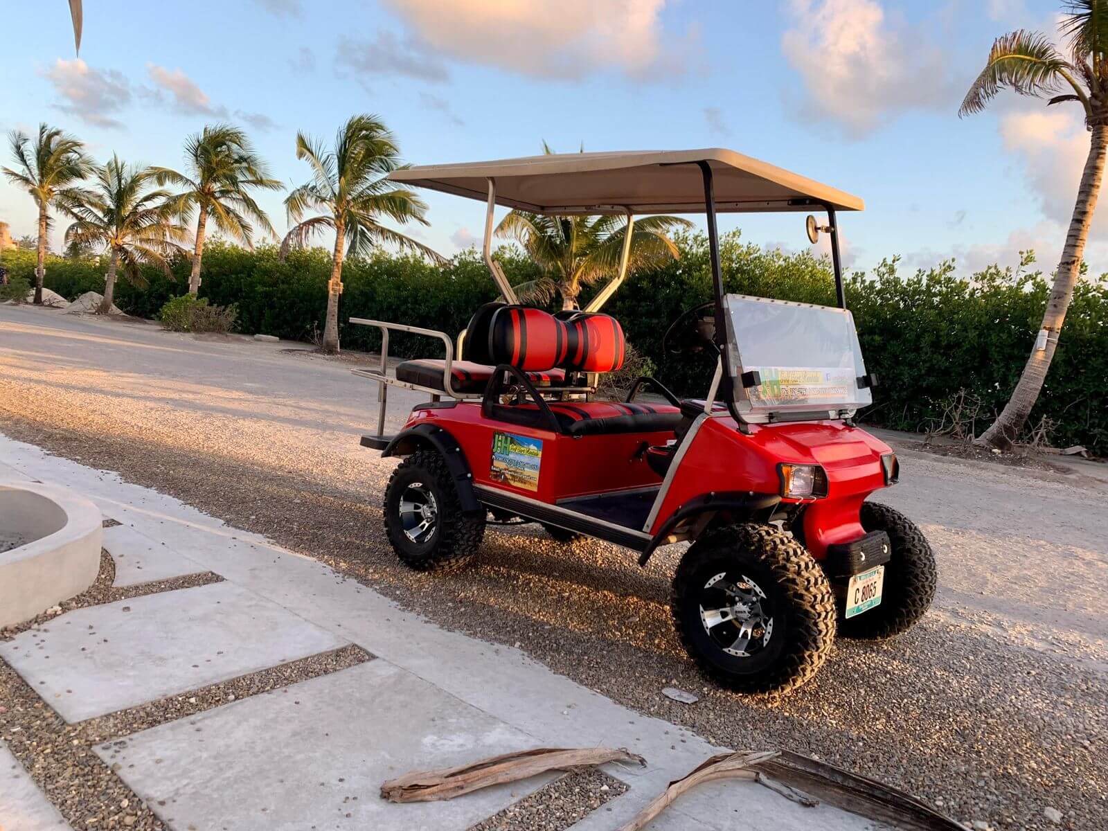Red golf cart parked among palm trees at golden hour on Ambergris Caye