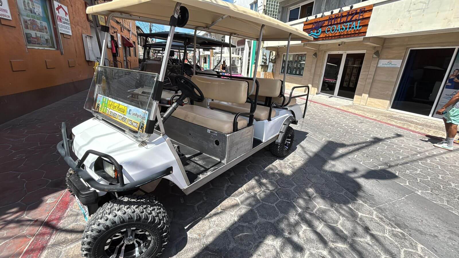White J and H golf cart with beige seats parked on a San Pedro street